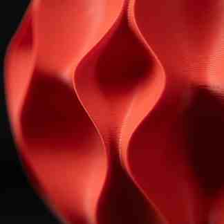 Close-up of intricate 3D-printed red geometric structure with smooth curves and fine details.