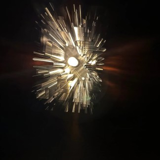 A sleek metallic 3D printed artwork illuminated by bright lighting, highlighting intricate details and craftsmanship.