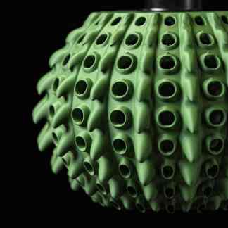 Close-up of a vibrant green 3D-printed lamp with pearl-like spikes on a black background.