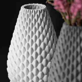A white 3D-printed vase with textured honeycomb design holding pink flowers, ideal for contemporary interior decoration.