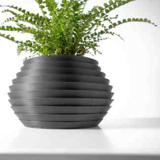 3D printed black flower pot with layered design and lush green plant.