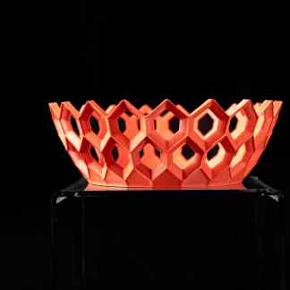 Intricate orange 3D-printed hexagonal bowl on clear pedestal, showcasing advanced additive manufacturing techniques.