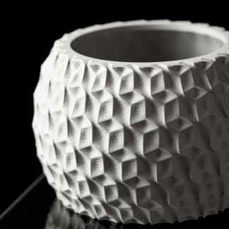 Detailed close-up of a white, honeycomb-patterned 3D-printed vase on black background.