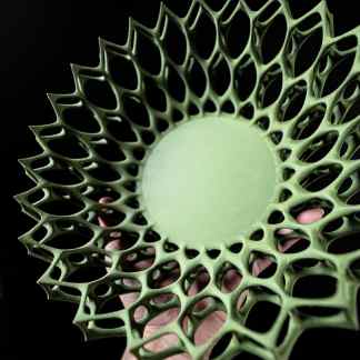 3D printed lattice structure in green with complex geometric pattern on black background.