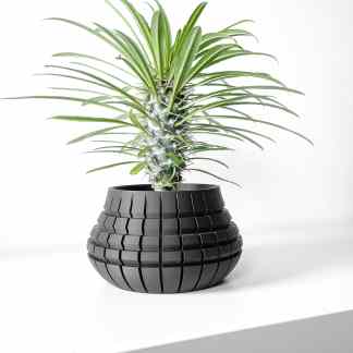 A sleek black 3D-printed vase with a contemporary geometric pattern featuring a green plant.