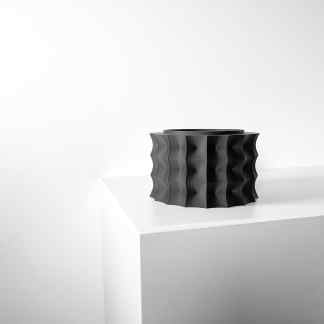 Modern black 3D printed vase with geometric patterns on a white pedestal.