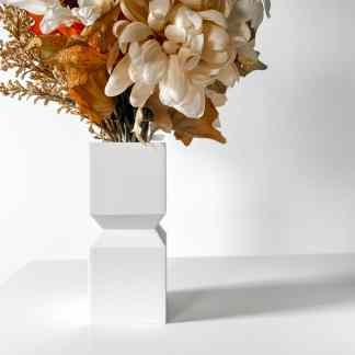 Elegant white geometric vase with faux flowers and leaves for home decor.