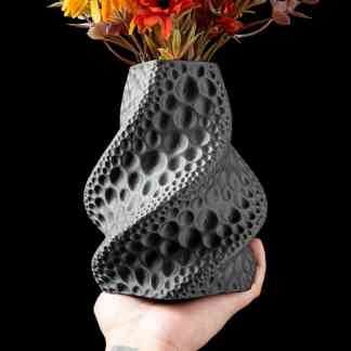 A modern black vase featuring a unique textured surface, holding colorful artificial flowers against a black background.