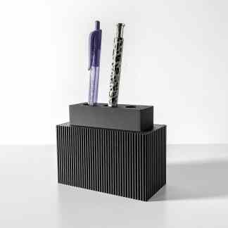 A modern black and gray pen holder featuring two stylish pens on a white desk. Sleek, functional desk accessory for organization.