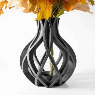 A modern black 3D printed vase with intricate openwork design holding colorful autumn leaves.