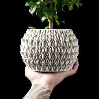 A close-up of a 3D-printed ceramic plant pot with a detailed geometric pattern held in hand.