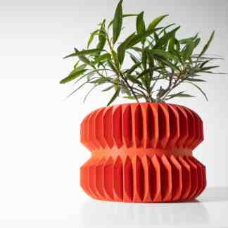 A vibrant orange 3D-printed planter with geometric ridges, featuring a lush green plant against a minimal white background.