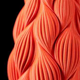 Bright orange 3D printed art piece with detailed textured design on black background.
