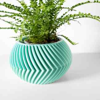 A turquoise 3D printed planter with a detailed, textured geometric pattern holding a lush green fern.