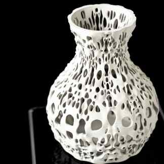 Intricate white 3D printed vase with complex lattice structure on black background.