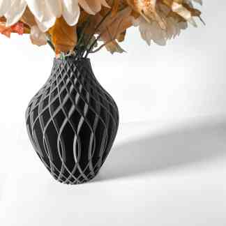 Black 3D-printed vase with intricate lattice pattern, holding dried flowers, on a white surface.