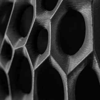 Close-up of a black 3D-printed metallic honeycomb or hexagonal lattice with intricate layers.