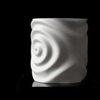 Close-up of a 3D-printed white ceramic coaster with spiral wave pattern on a black background.