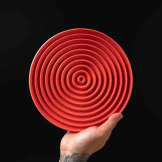 Hand holding a vivid red concentric circle sculpture against black background.