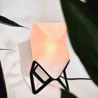 Modern origami-inspired table lamp with soft pink glow and black geometric stand.